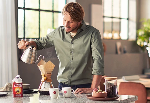 man die aan de keuken met een metalen kan koffie zet via een koffiefilter.
