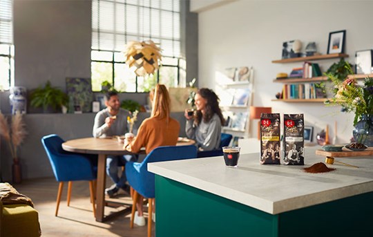 Drinkende mensen in een woonkamer met Douwe Egberts Café koffiebonnen op het aanrecht.