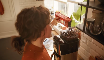 Vrouw die koffiebonen in een koffiezetapparaat doet.