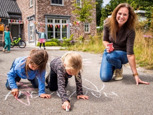 A mother and two children with sidewalk chalk playing on the streets.
