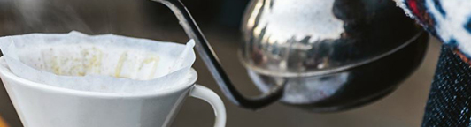 Koffie die geschonken wordt in een koffiemok met een koffiefilter erin.