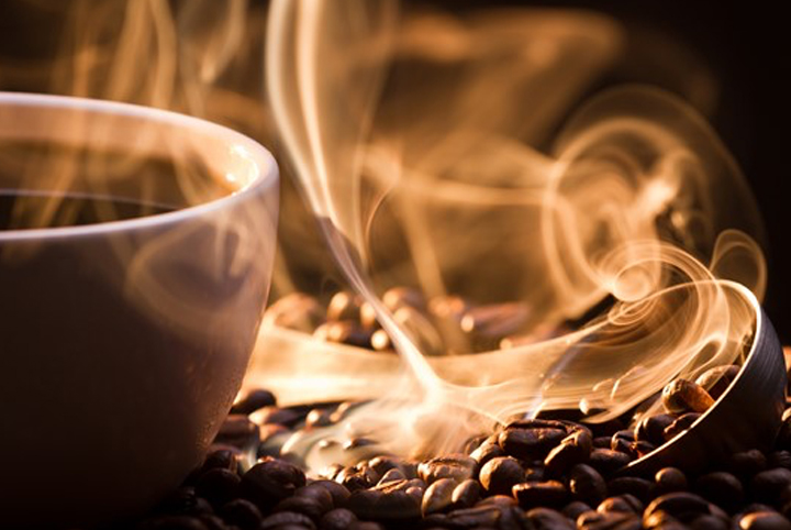 Koffiebonen naast een koffiemok waarvan de aroma af komt.