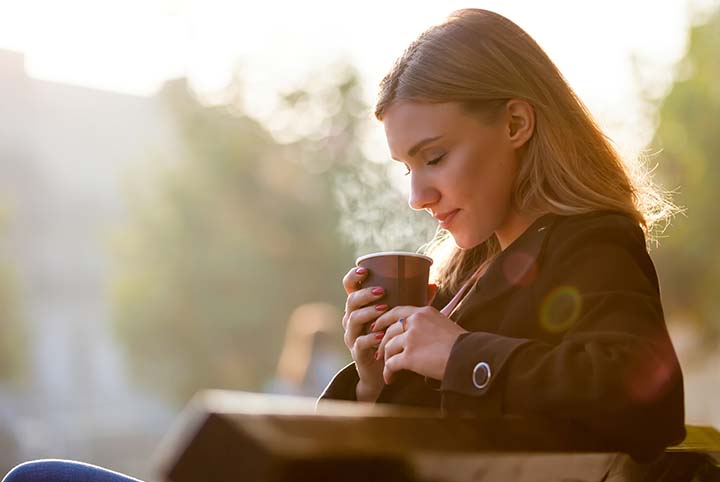 Vrouw die buiten op een bankje zit en koffie drinkt.
